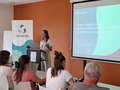 A speaker presents to an audience in a meeting room. A Viaverda banner stands beside a projection screen displaying a presentation.