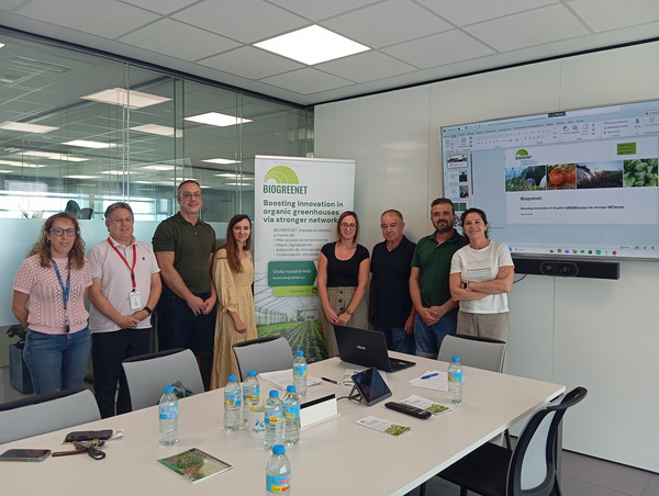 Eight people standing in a meeting room beside a BIOGREENET banner and presentation screen.