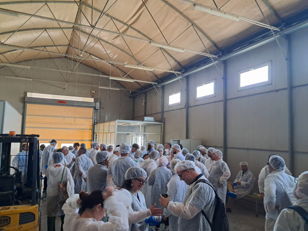 A group of people stands in a hall, wearing white hygienic coveralls and hairnets.