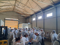 A group of people stands in a hall, wearing white hygienic coveralls and hairnets.