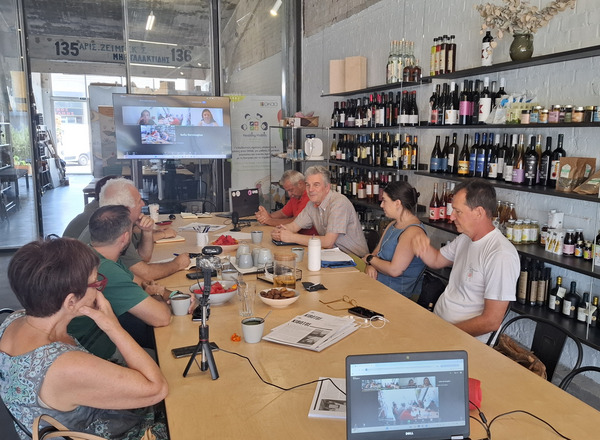 Group of people sitting on a table with a laptop and people in an online meeting.